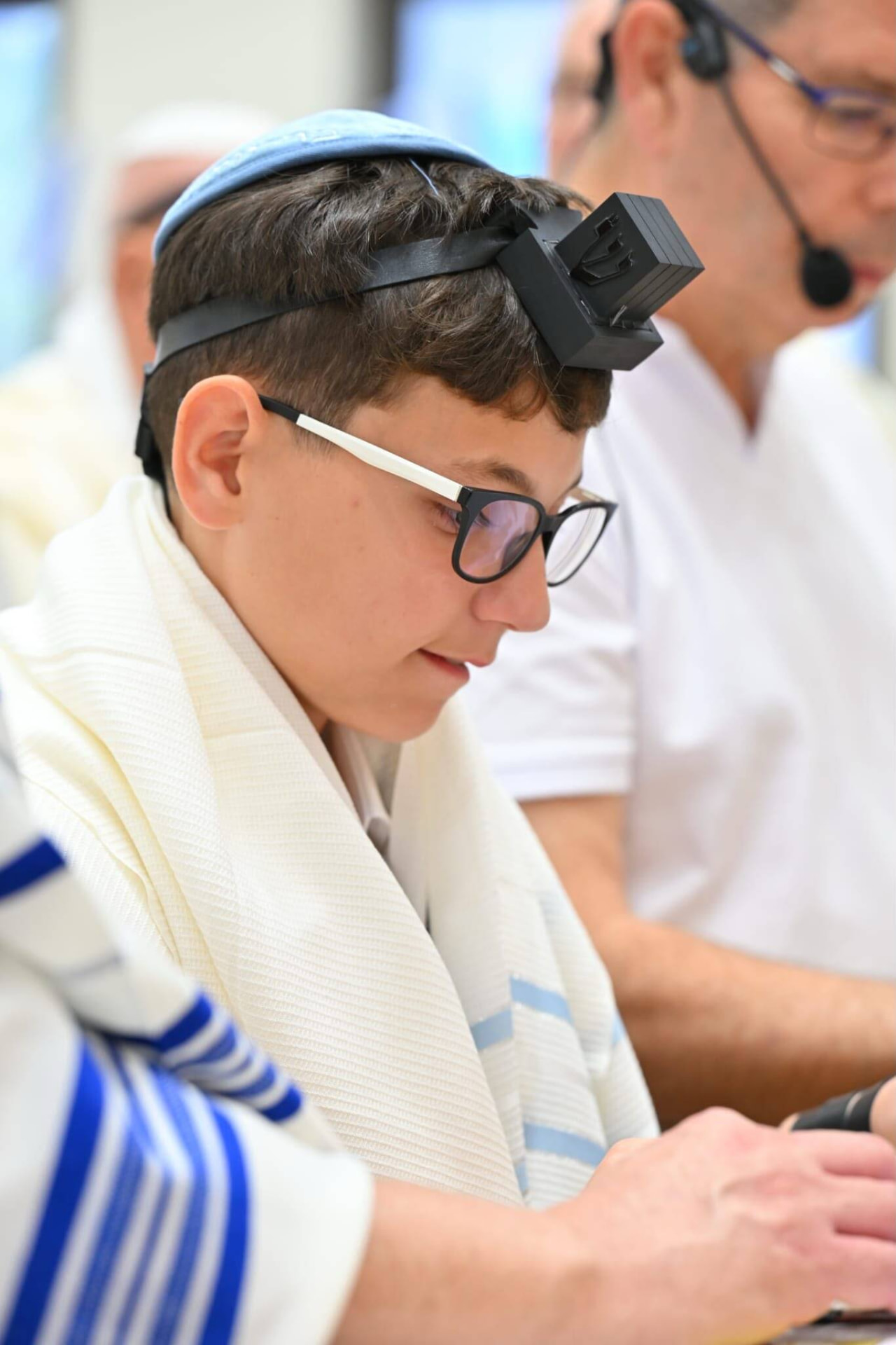 נער בר מצווה עוטה טלית ותפילין מרוכז בקריאה