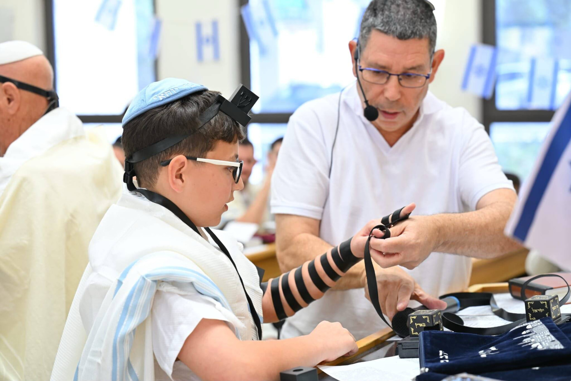 עמיחי מלמד את הנער לכרוך תפילין על היד בבית הכנסת